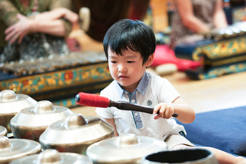 A young Asian boy playing the metal percussion instruments with a mallet.